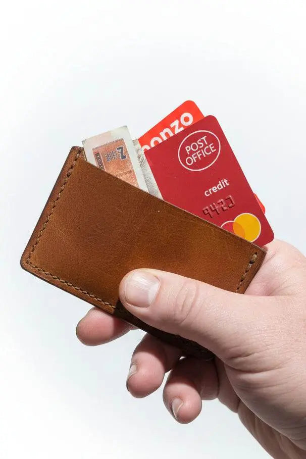 Hand holding a slim handmade tan leather card sleeve filled with cards and cash