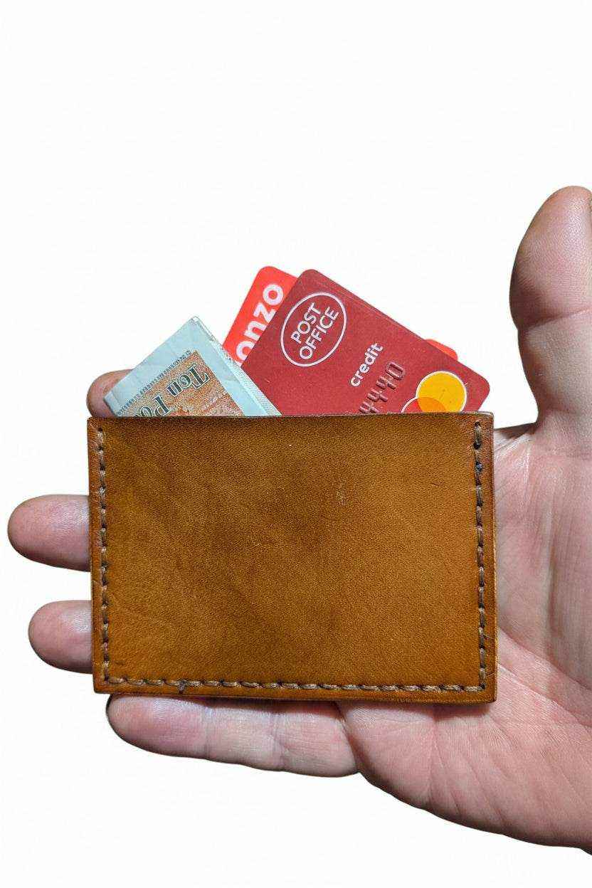 Handmade tan leather card sleeve held in a hand with cards inside