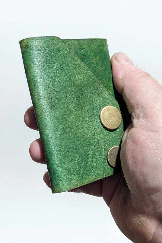 Handmade green leather wallet with brass snap closures held in a hand.