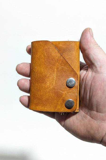 The Club tan leather cash fold wallet with two snap closures, held in hand