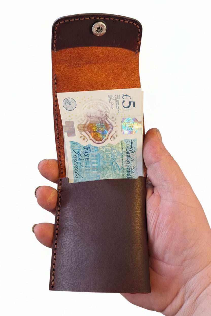 Handmade brown leather slim wallet holding a five pound note held by a hand.