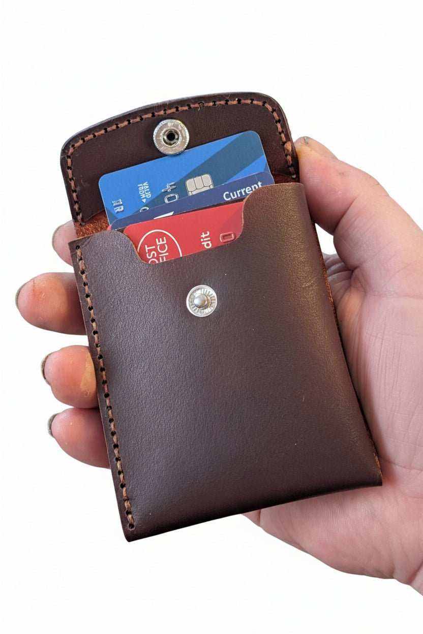 Slim dark brown leather money fold with snap flap, holding bank cards