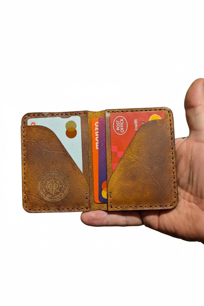 Handmade brown leather bi-fold wallet held in a hand, filled with credit cards.