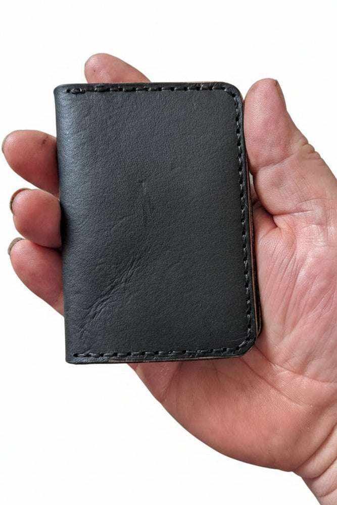 The Devonport black leather bi-fold wallet closed, held in hand