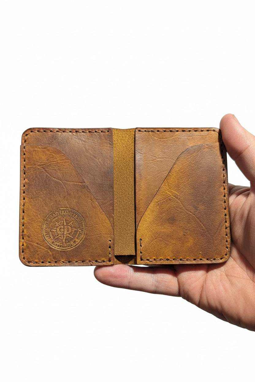 Handmade brown leather bifold wallet held in a hand, featuring a stamped circular logo.