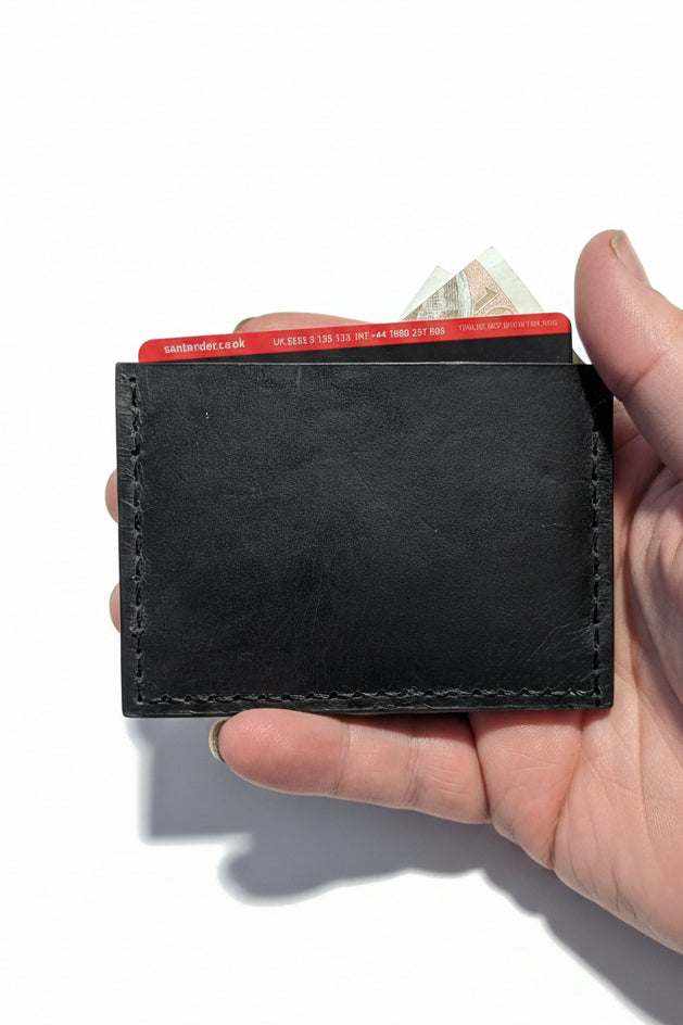 Handmade black leather card holder being held with credit cards and cash inside.