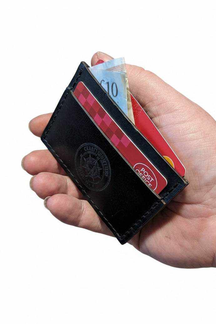 Handmade black leather card holder wallet containing credit cards and cash.