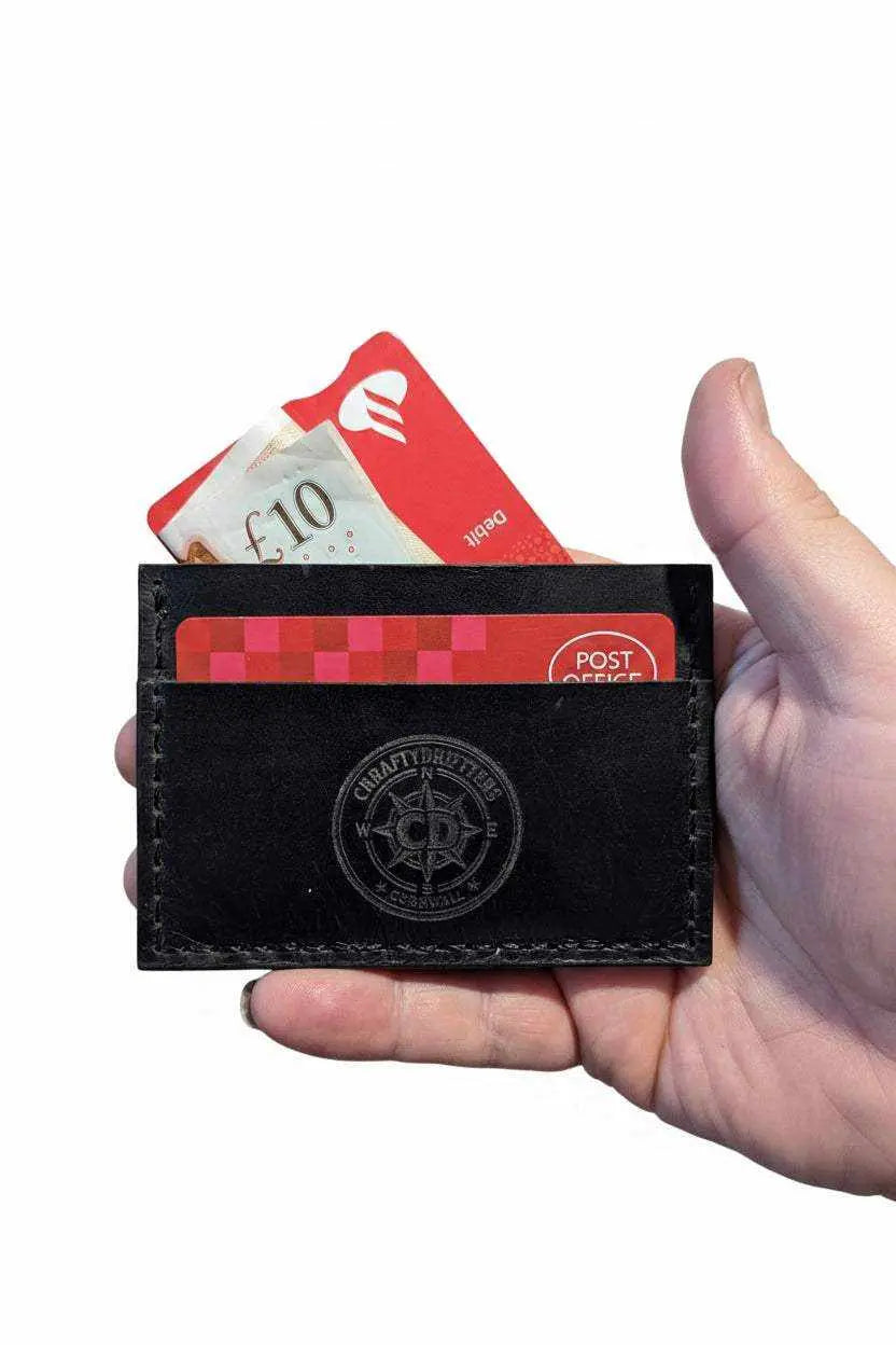 Hand holding a slim black handmade leather card holder with a ten pound note and red debit card.