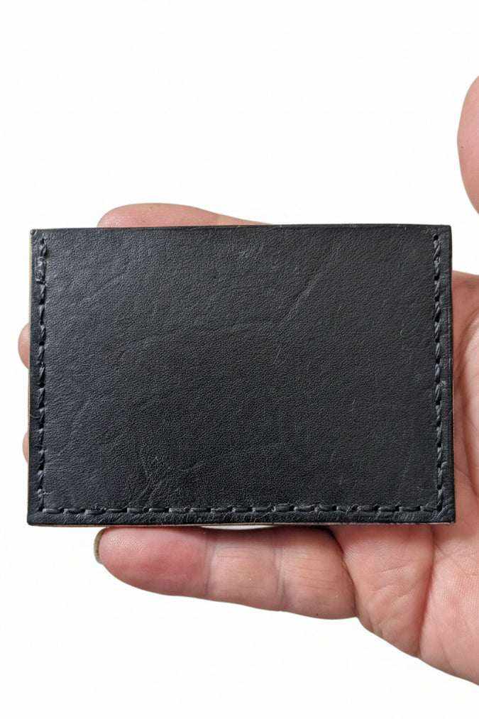 Handmade black leather card holder with visible perimeter stitching held in hand.