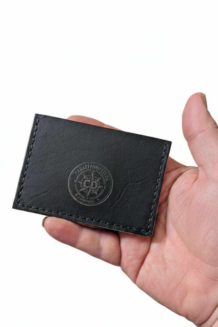 Handmade black leather card holder with embossed logo held in a person's hand.