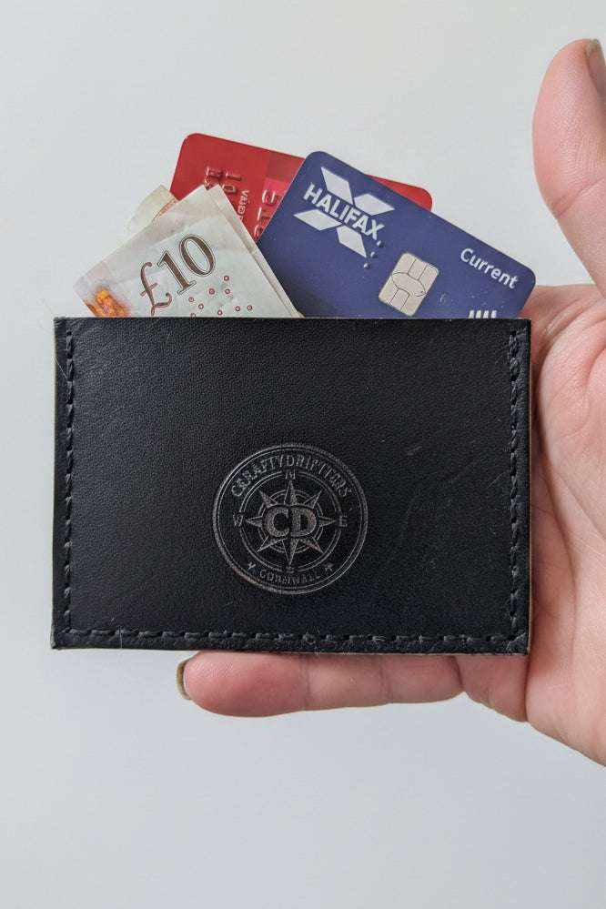 Handmade black leather card holder with embossed logo containing bank cards and cash.
