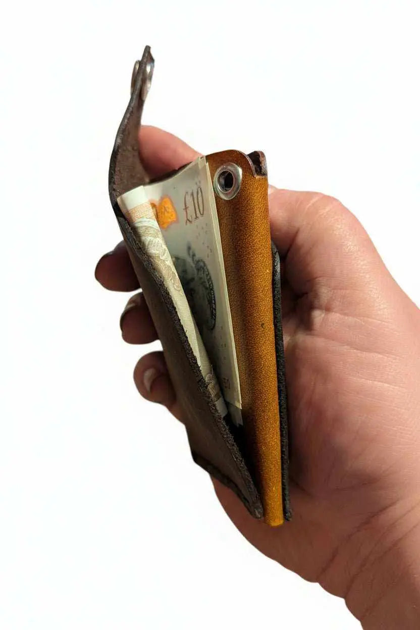 Hand holding a handmade brown leather wallet containing a ten pound note.