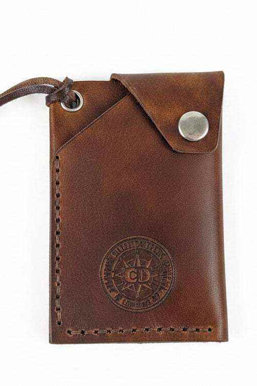 Handmade brown leather card holder with a snap button closure and embossed logo.