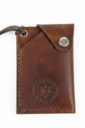 Handmade brown leather card holder with a snap button closure and embossed logo.