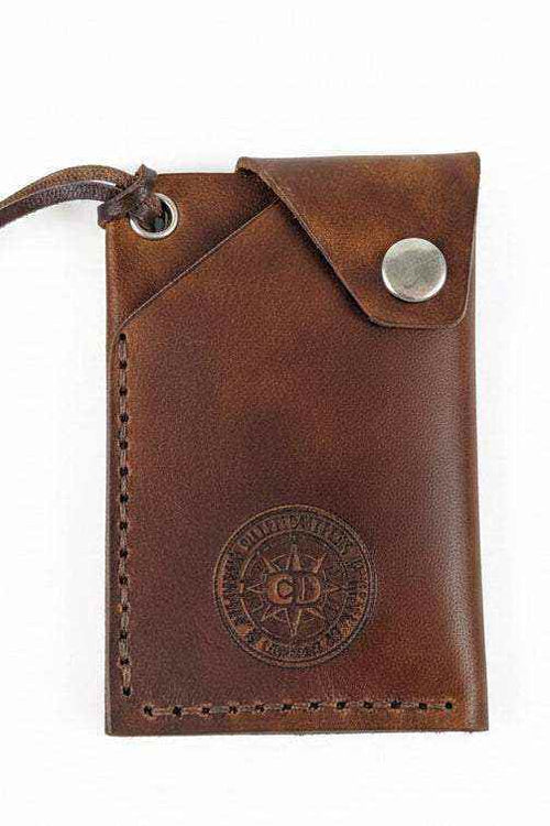 Handmade brown leather card holder with a snap button closure and embossed logo.
