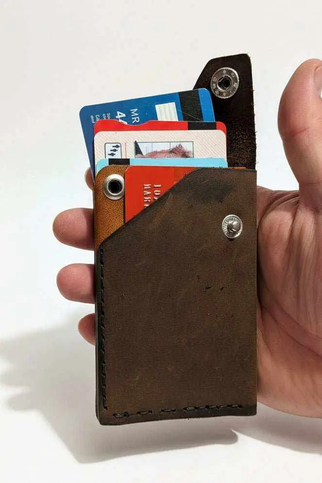 Handmade brown leather card holder with credit cards held in a person's hand.