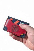 Hand holding a handmade red and navy blue leather card holder with card slots.