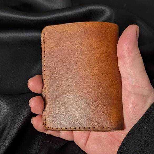 The Hilldown tan leather bi-fold wallet closed in hand, showing the hand stitching
