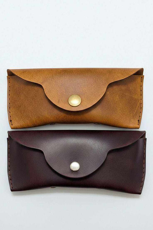 Handmade leather eyewear cases in tan and dark brown with metal snap closures.