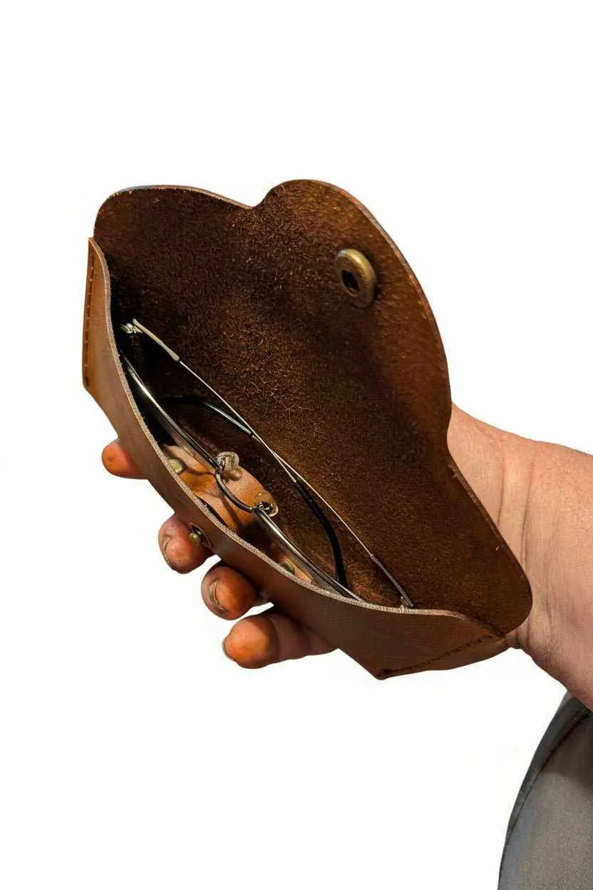 Handmade brown leather glasses case held in hand against a white background.