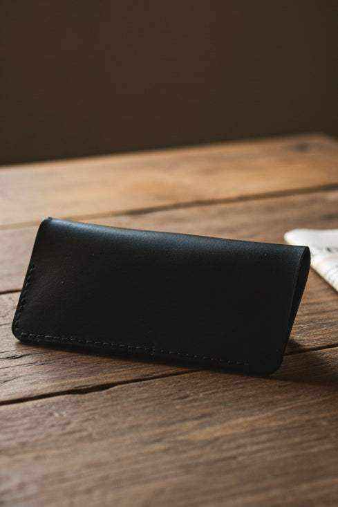 Handmade black leather glasses sleeve resting on a rustic wooden surface