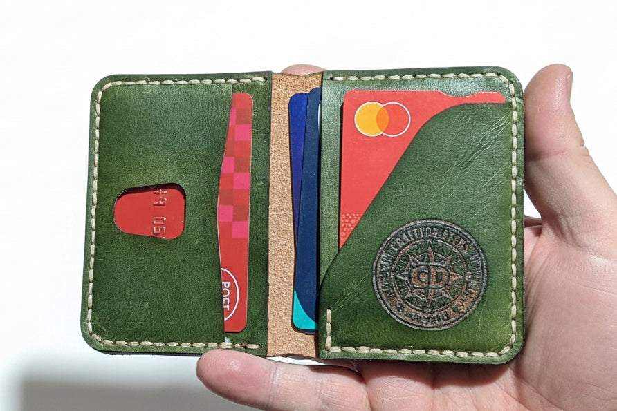 Handmade green leather bi-fold wallet holding credit cards held in a hand.