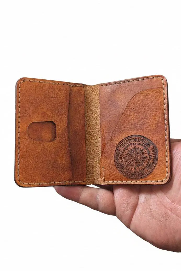 Handmade tan leather bifold wallet held in hand, featuring a vintage compass logo stamp.