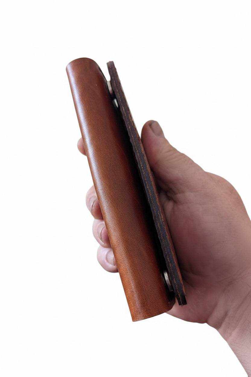 Hand holding a slim, handmade brown leather Darts case showing its side profile.