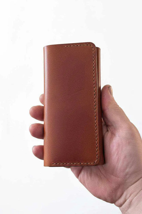 Hand holding a handmade brown leather Darts Case with visible stitching.