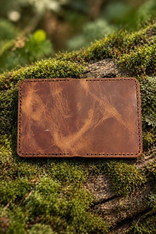 Devonport Premium tan Badalassi leather bi-fold closed on moss, showing the pull-up grain