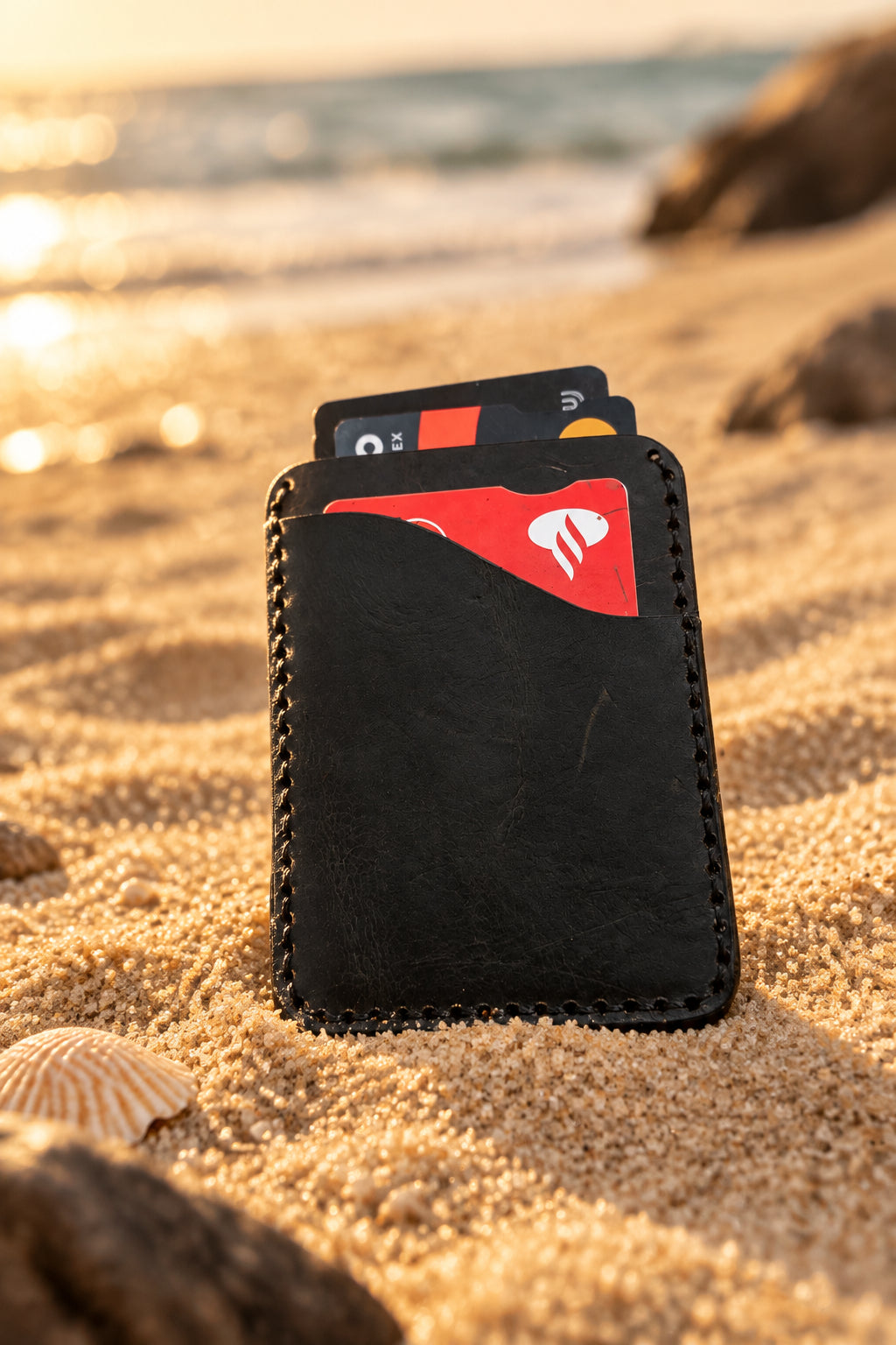 Black Badalassi leather card holder holding bank cards, on sand at sunset