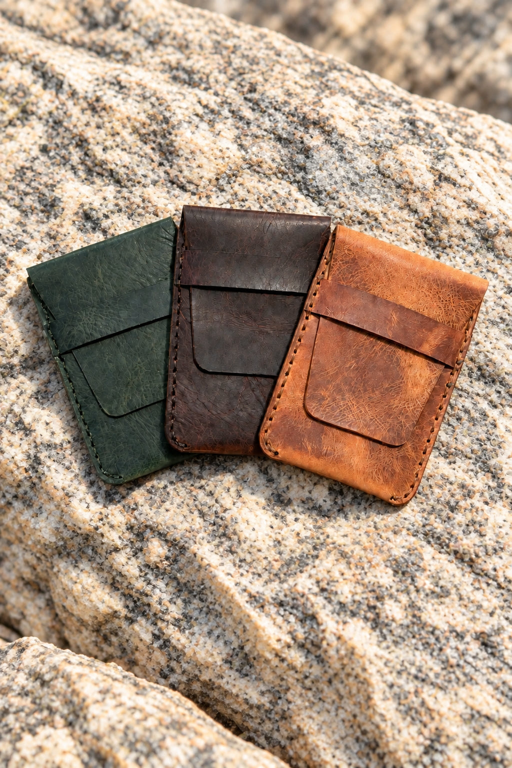 Green, dark brown and tan Badalassi Carlo leather card sleeves side by side on a rock