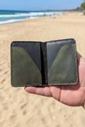 Handmade two-tone black and olive green leather minimalist wallet held on a sandy beach