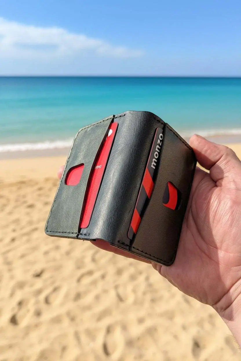 Hand holding a handmade black leather card wallet with Monzo cards on a sunny beach.