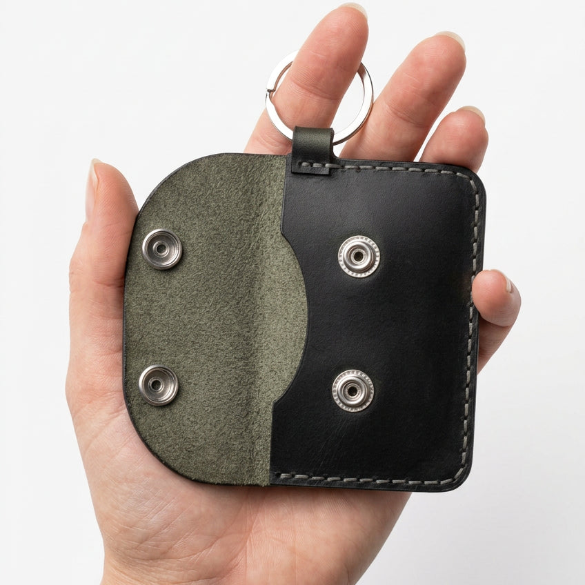 Black leather keyring card and cash purse with grey flap, held open in hand