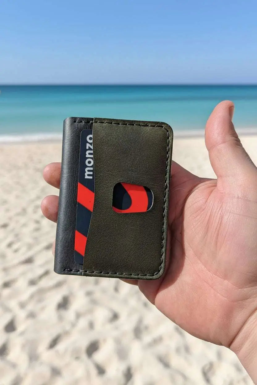 The Devonport Plus olive green and black leather bi-fold closed, held on a beach