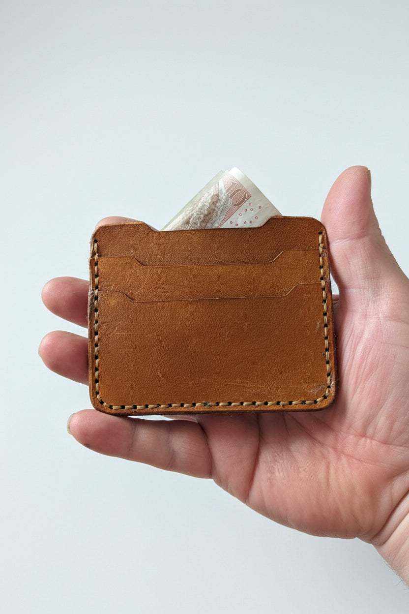 Handmade brown leather card holder with cash held in a person's hand.