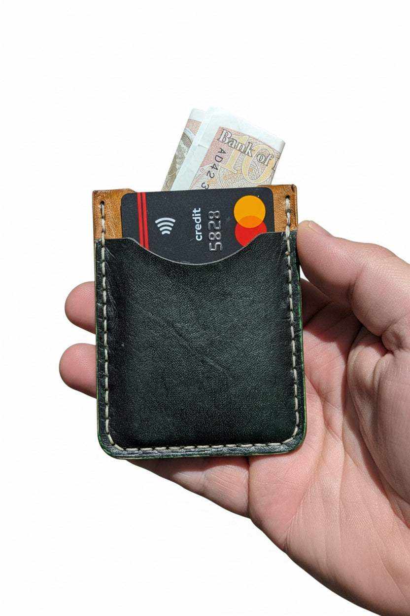 Handmade black leather card holder with cash and credit card held in hand.