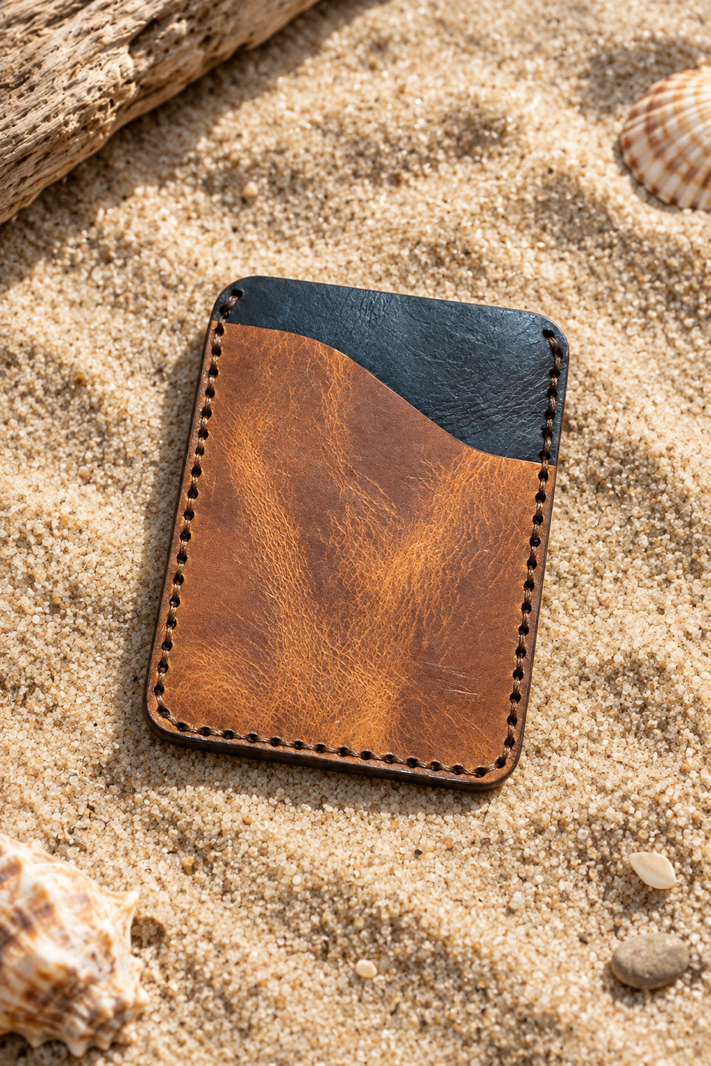 Tan and navy Badalassi leather card holder on sand, front view
