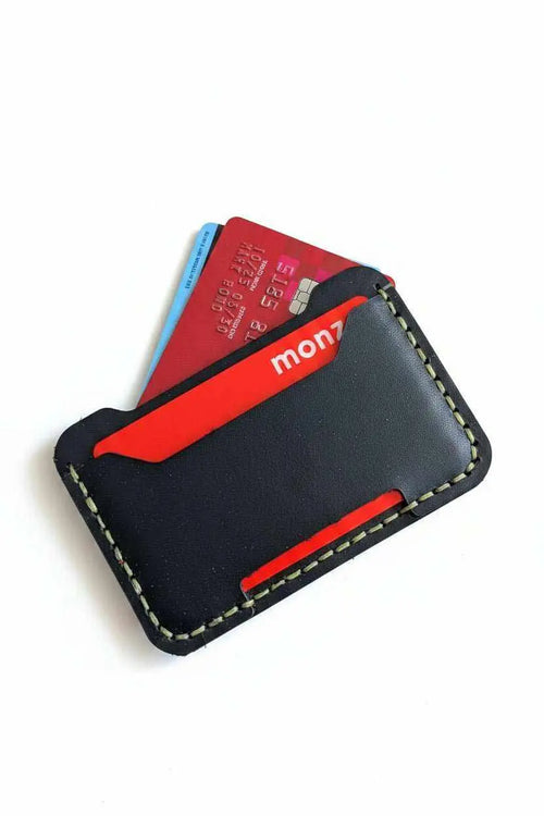 Handmade black leather minimalist card holder with red accent containing credit cards.