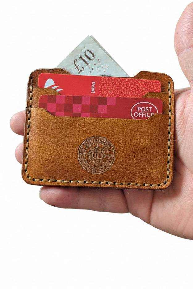 Handmade tan leather card holder with bank cards and a ten pound note held in hand.
