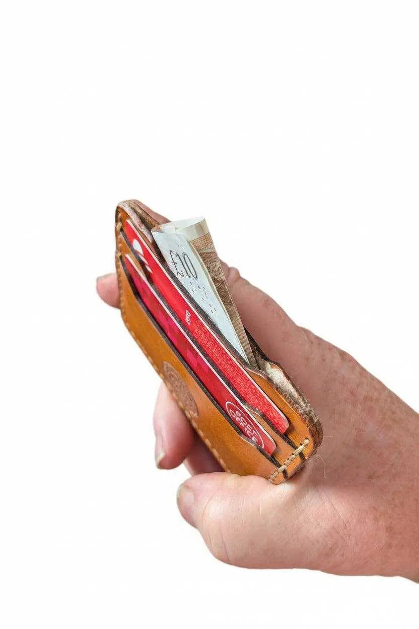 Hand holding a slim handmade leather wallet containing cash and credit cards.
