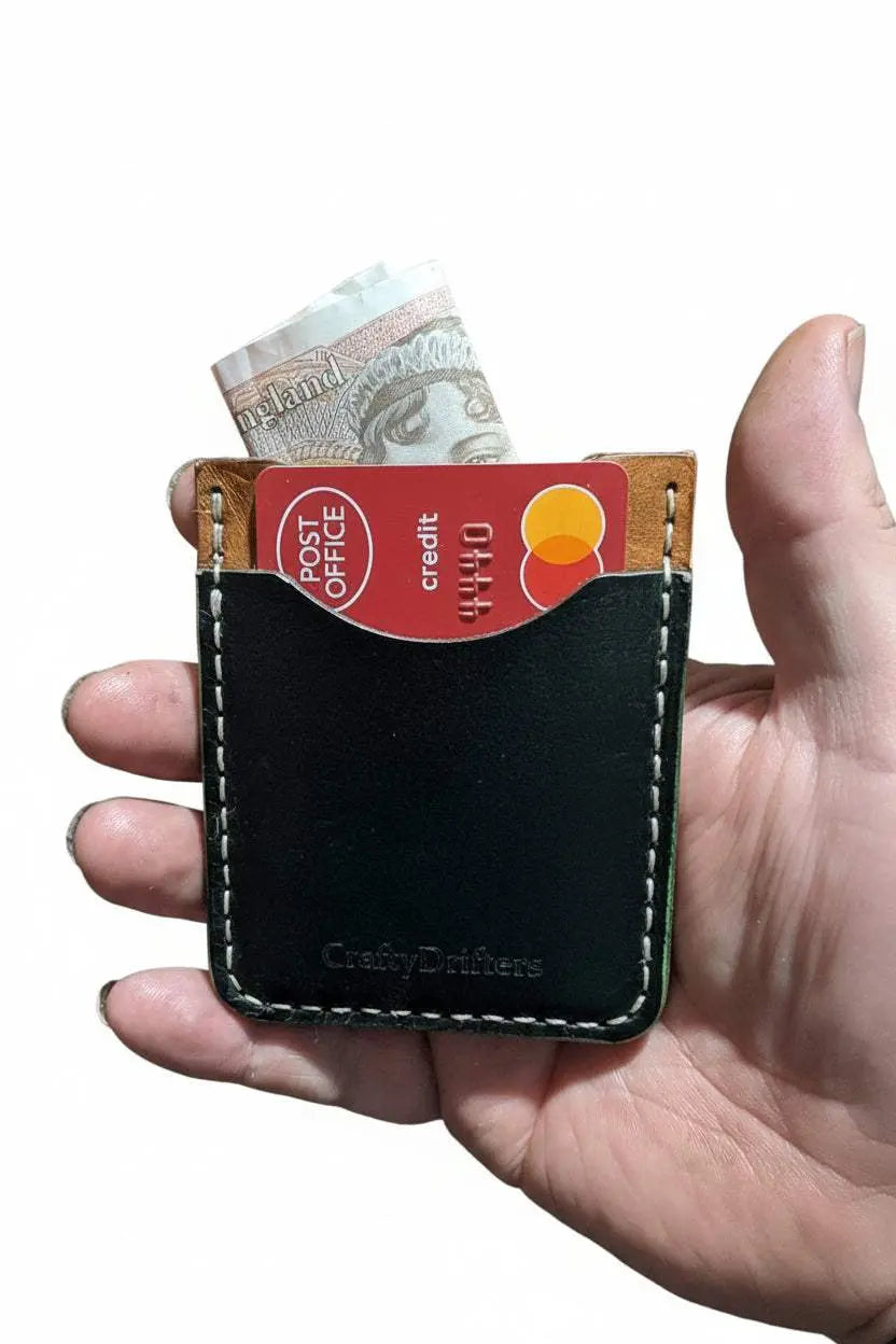 Handmade black leather card holder with cash and credit cards held in a hand.