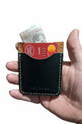 Handmade black leather card holder with cash and credit cards held in a hand.