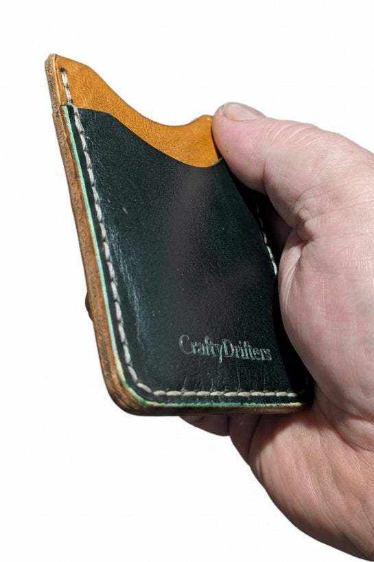 Handmade black leather card holder with tan trim and white stitching held in a hand.