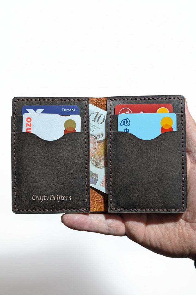 The Fistral dark brown leather bi-fold wallet open with bank cards and cash, held in hand
