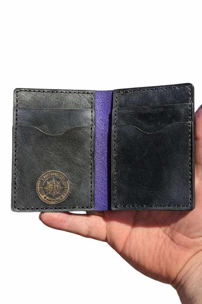 The Fistral bi-fold wallet open, dark leather with purple lining and compass logo