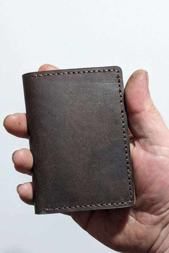 Handmade dark brown leather wallet with rustic stitching held in a person's hand.
