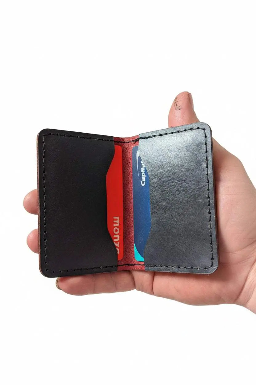 Handmade black leather card holder wallet holding credit cards held in a hand.