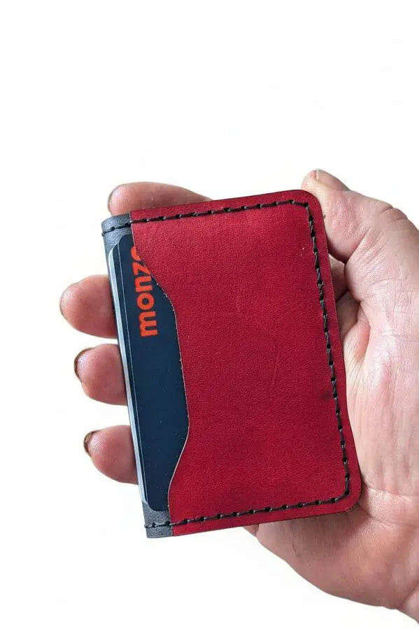 Hand holding a handmade red leather card holder with a black debit card inside.